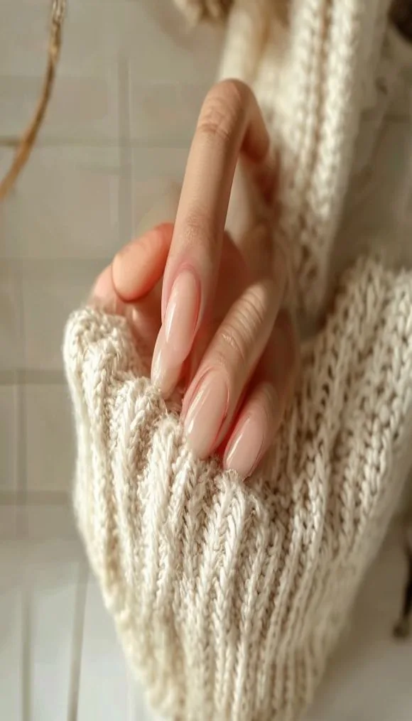 Close-up of a manicured hand in a warm neutral fall nail set, resting against a cream knit sweater